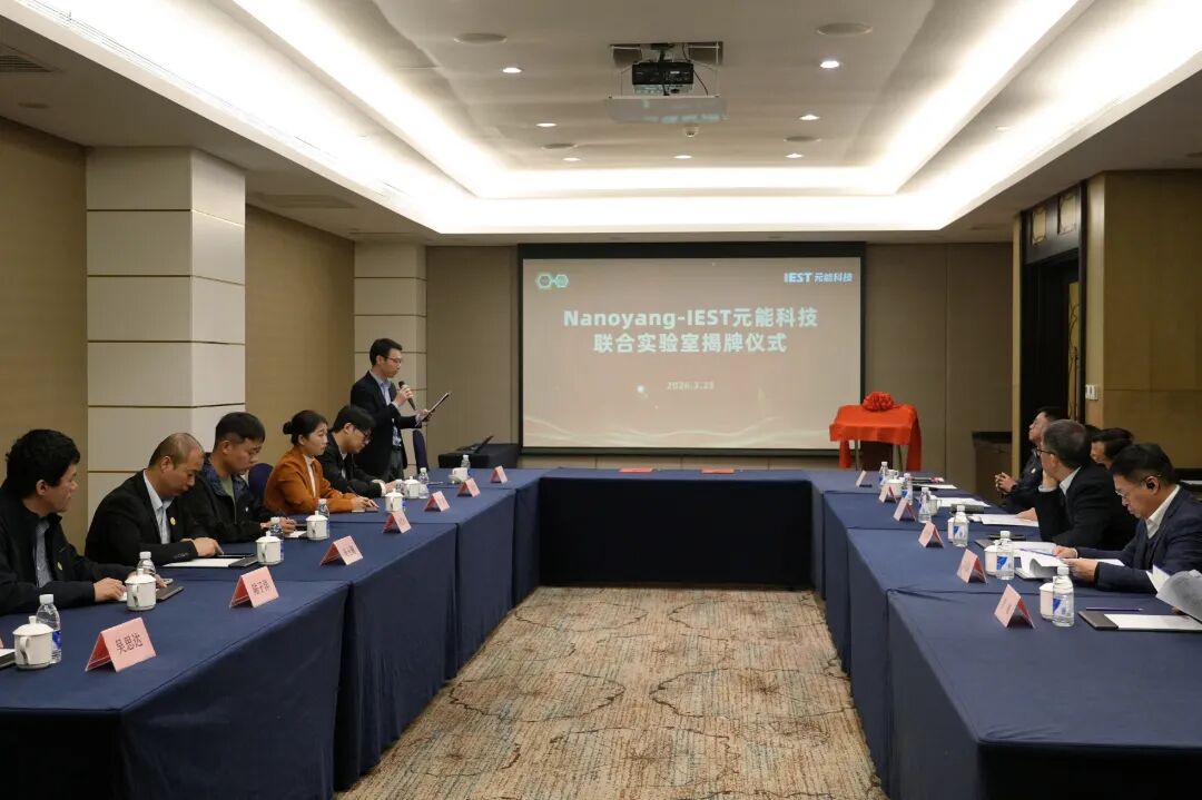 IEST Instrument and Nanoyang at Tianjin University Establish Joint Laboratory for Advanced Battery Research 3 Wide-angle view of the Nanoyang–IEST Instrument Joint Laboratory unveiling ceremony showing the projector screen displaying "联合实验室揭牌仪式" dated March 23, 2026, a plaque unveiling station with orange cloth, and approximately 12–14 attendees including academicians, professors, and IEST representatives seated around U-shaped tables